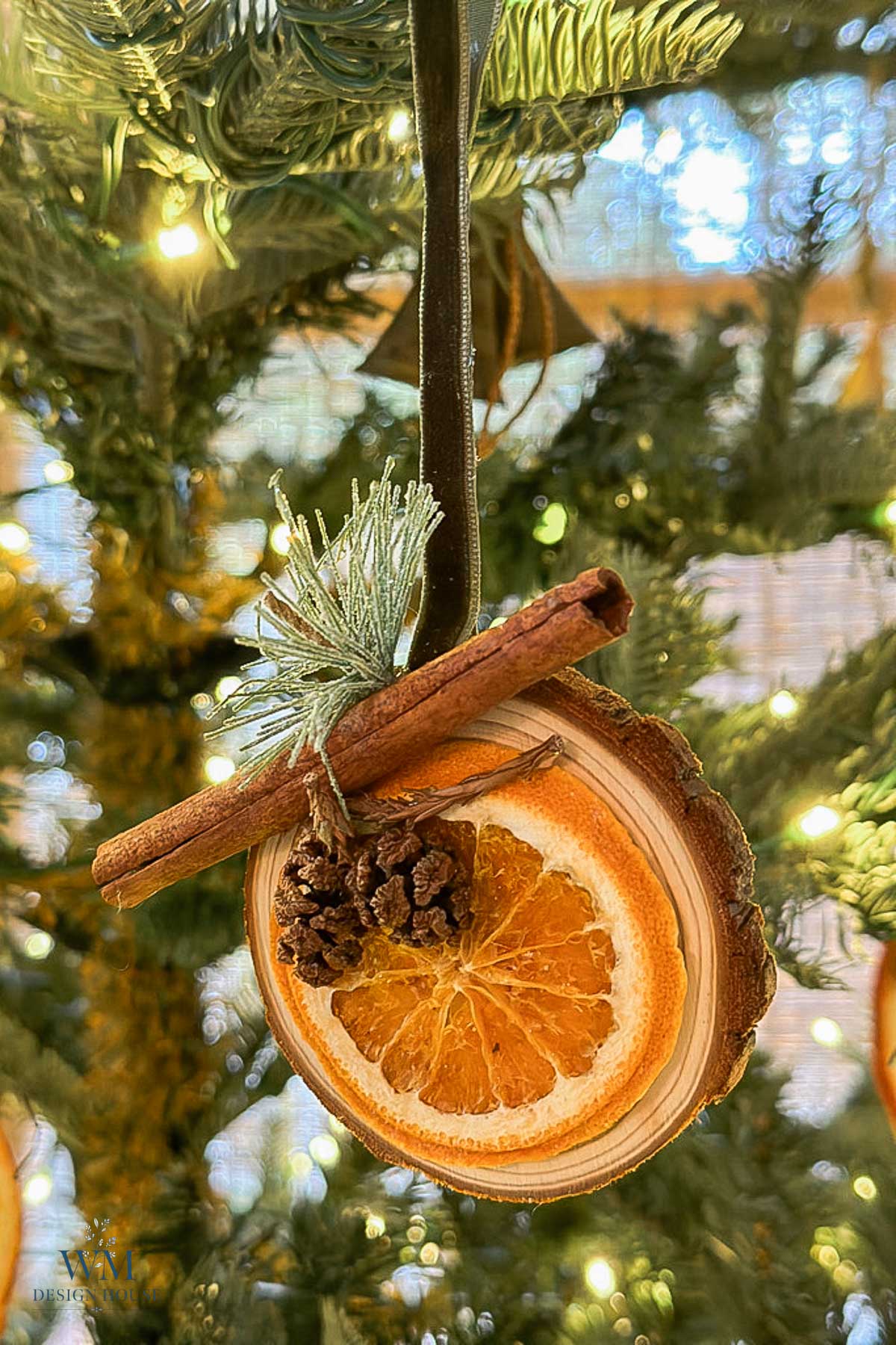 Christmas tree ornament made from a dried orange slice, a cinnamon stick, and a small pinecone hanging on a ribbon.