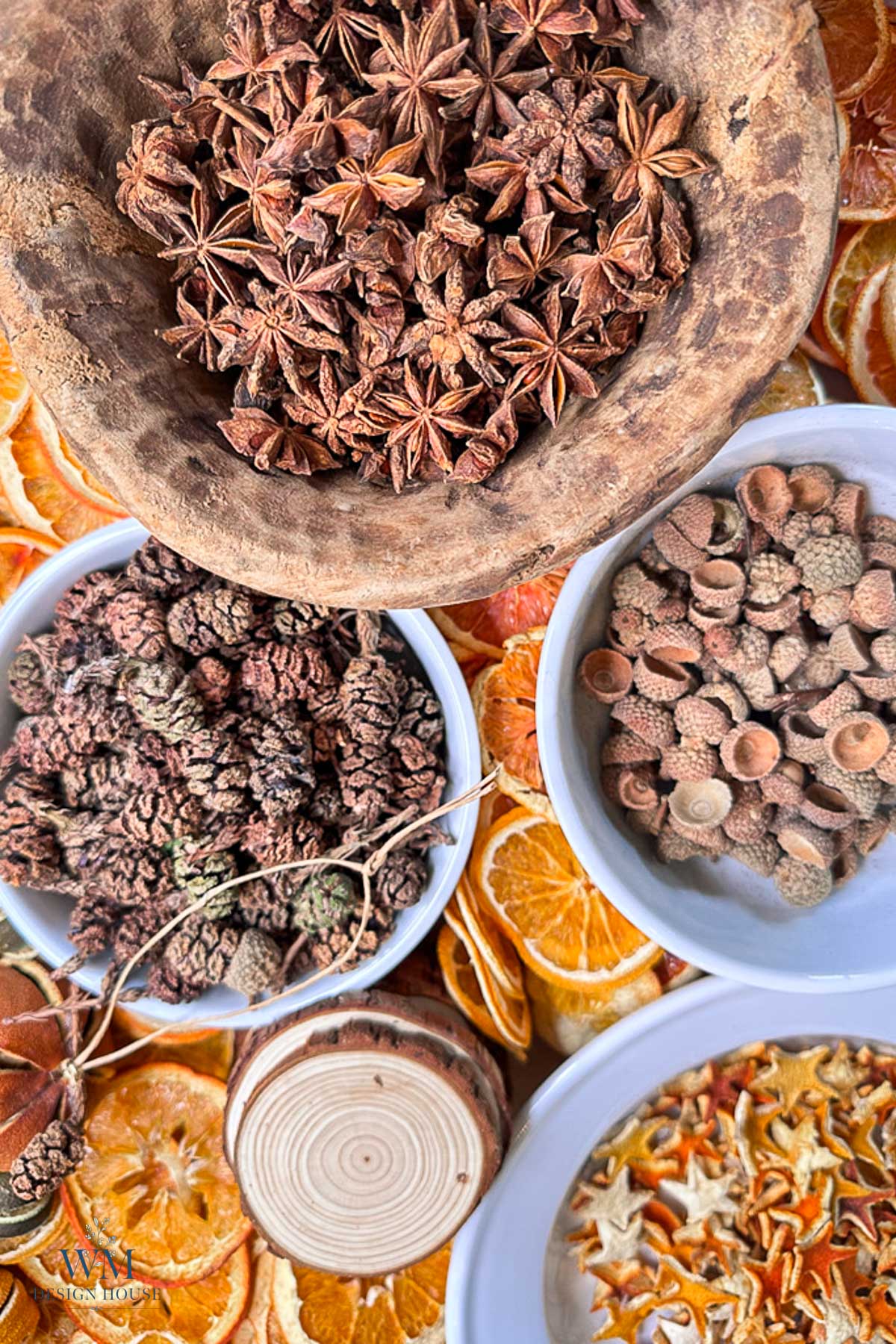 A wooden bowl of star anise, a bowl of small pinecones, a bowl of acorn caps, and a dish of dried orange slices and citrus peels.