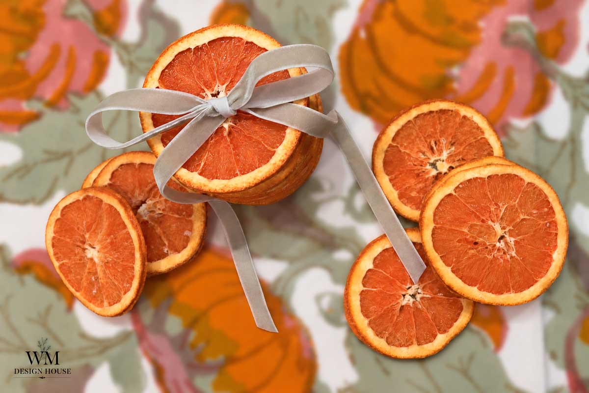 A stack of dried grapefruit slices tied with a grey velvet ribbon, surrounded by loose slices on a patterned surface.
