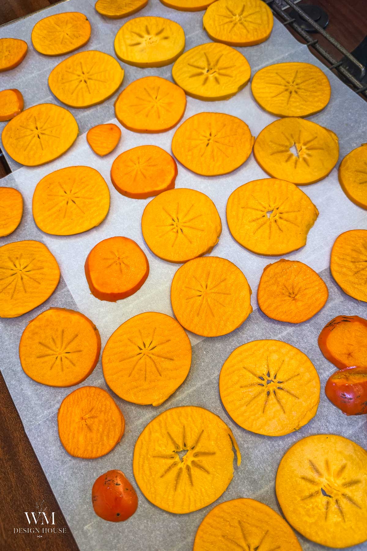 Slices of bright orange persimmon spread out on a parchment-lined baking sheet.