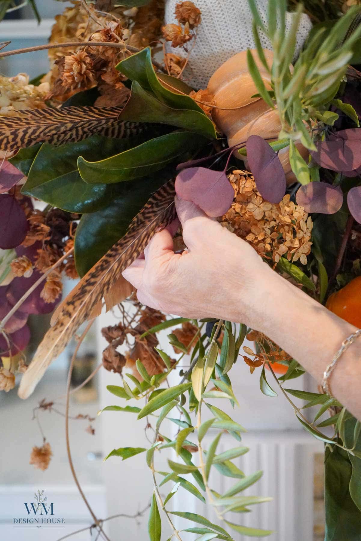 A person’s hand arranging feathers, dried flowers, and greenery into DIY fall decor.