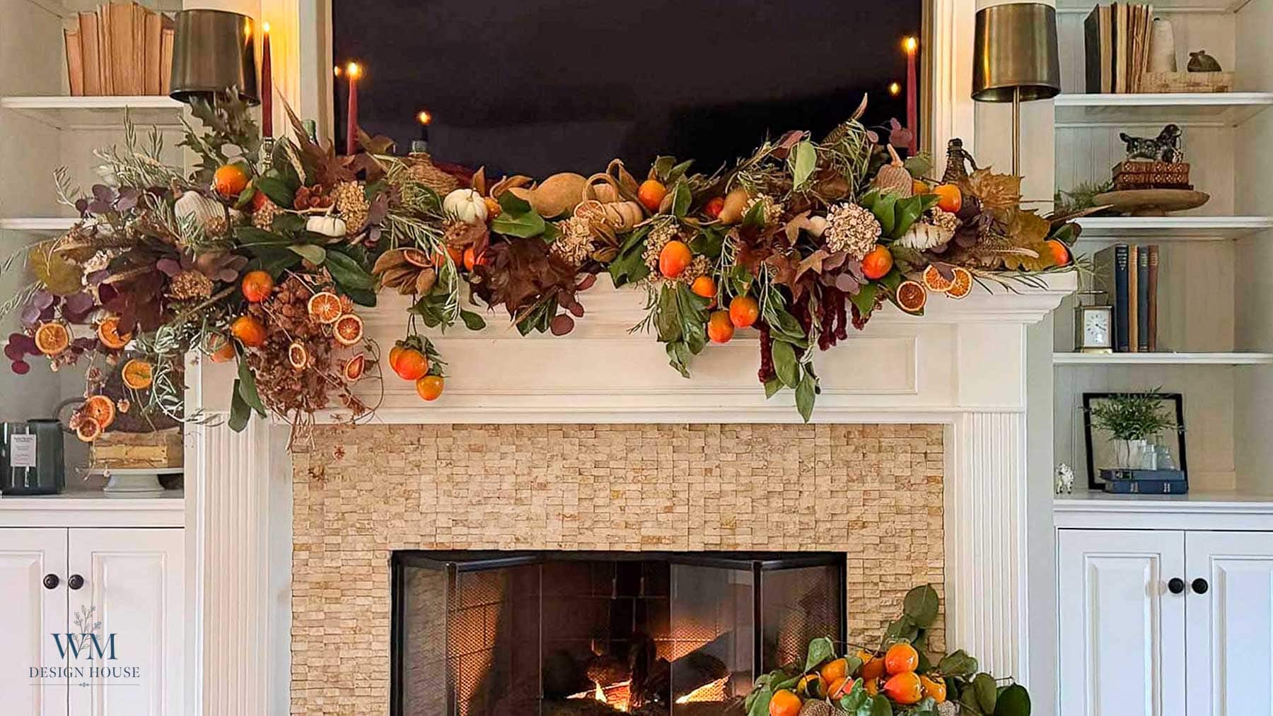 A fall mantel decorated with a garland of dried leaves, oranges, pumpkins, and candles for seasonal home decor.