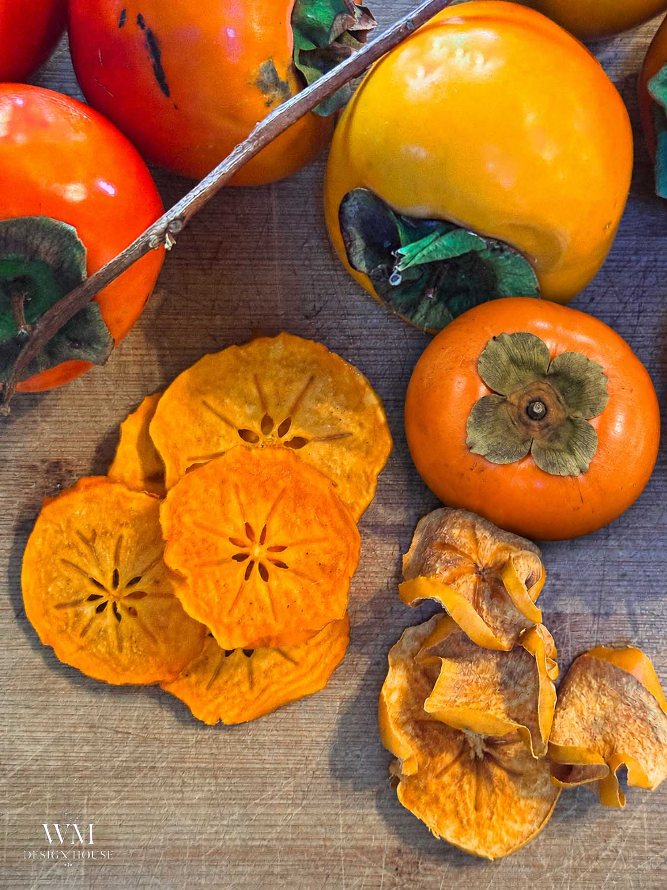 Whole Hachiya and Fuyu persimmons next to dried persimmon slices on a wooden surface.