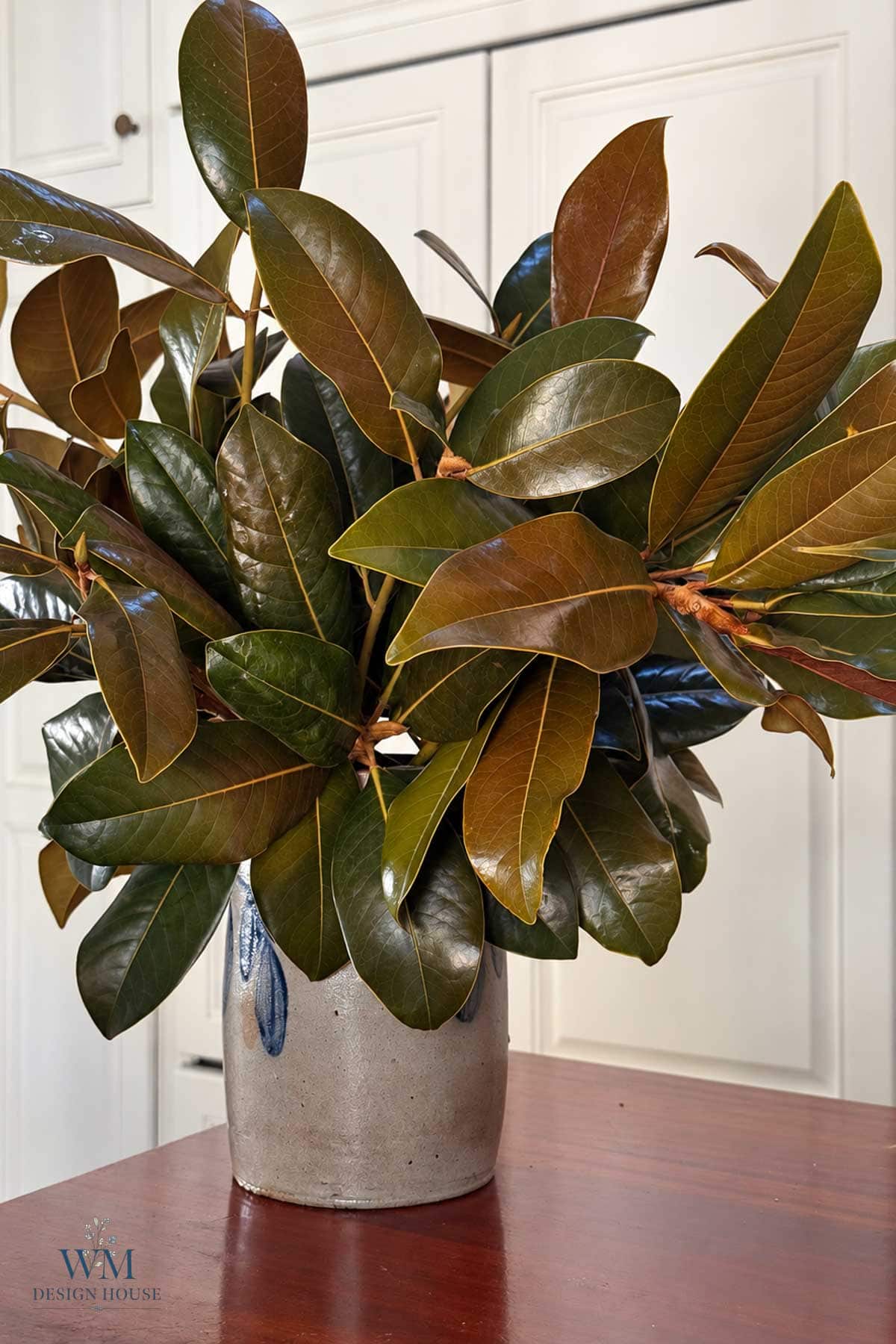 A large arrangement of magnolia branches in a speckled ceramic vase.