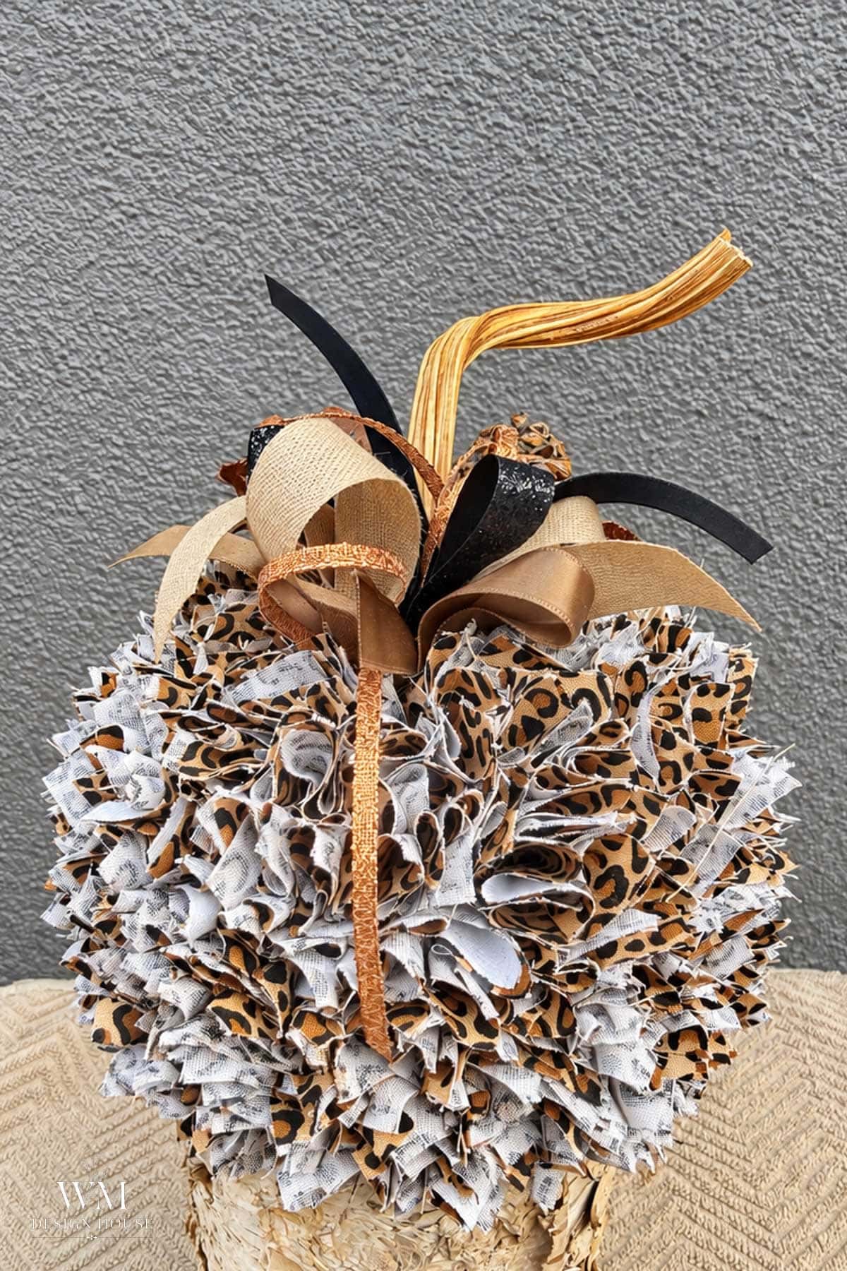 Decorative pumpkin made from layered fabric scraps in a leopard print. Topped with a cluster of gold, black, and tan ribbons with a natural pumpkin stem.