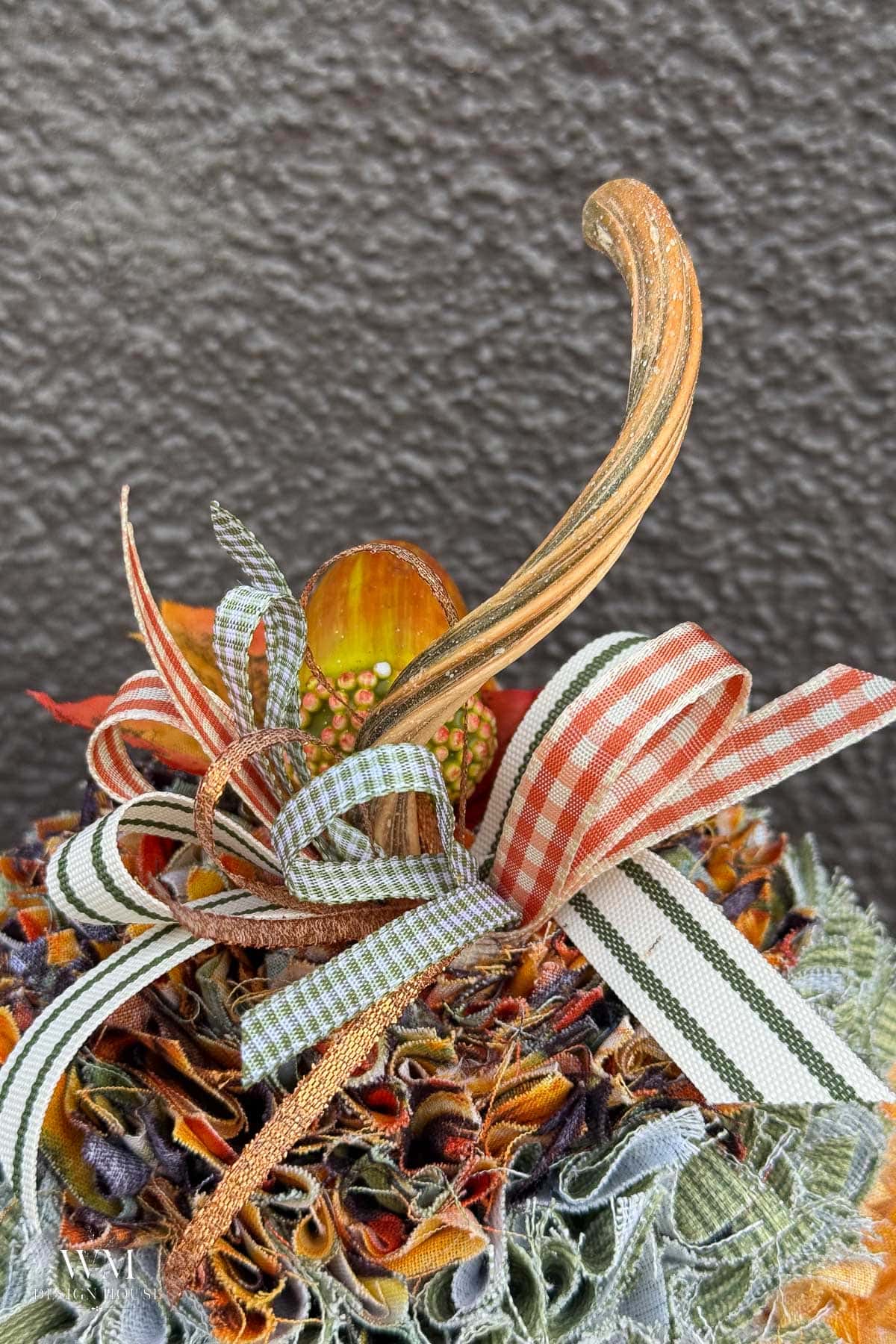 Decorative no sew fabric pumpkin topped with a long stem and a cluster of gingham and striped ribbons.