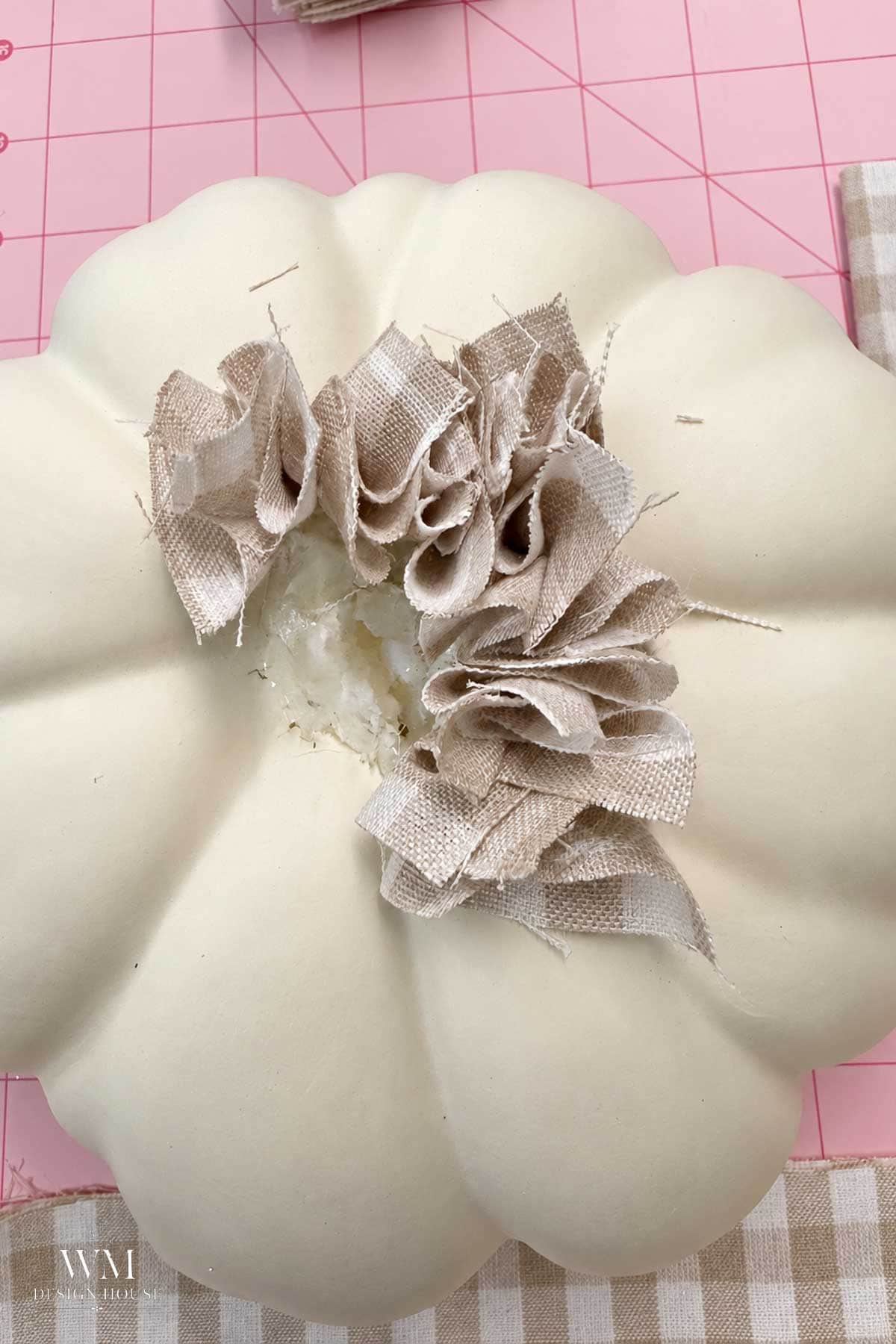 A craft project featuring a white faux pumpkin with a ruffled beige and white check fabric attached to the top.