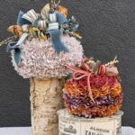 Two decorative no sew fabric pumpkins: one light-colored on a birch log pedestal and one red and purple on a vintage-style advertising box.