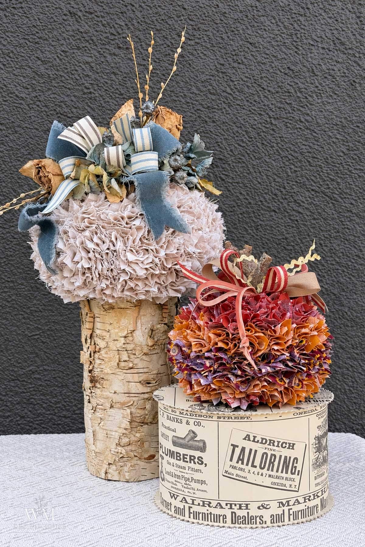 Two decorative no sew fabric pumpkins: one light-colored on a birch log pedestal and one red and purple on a vintage-style advertising box.