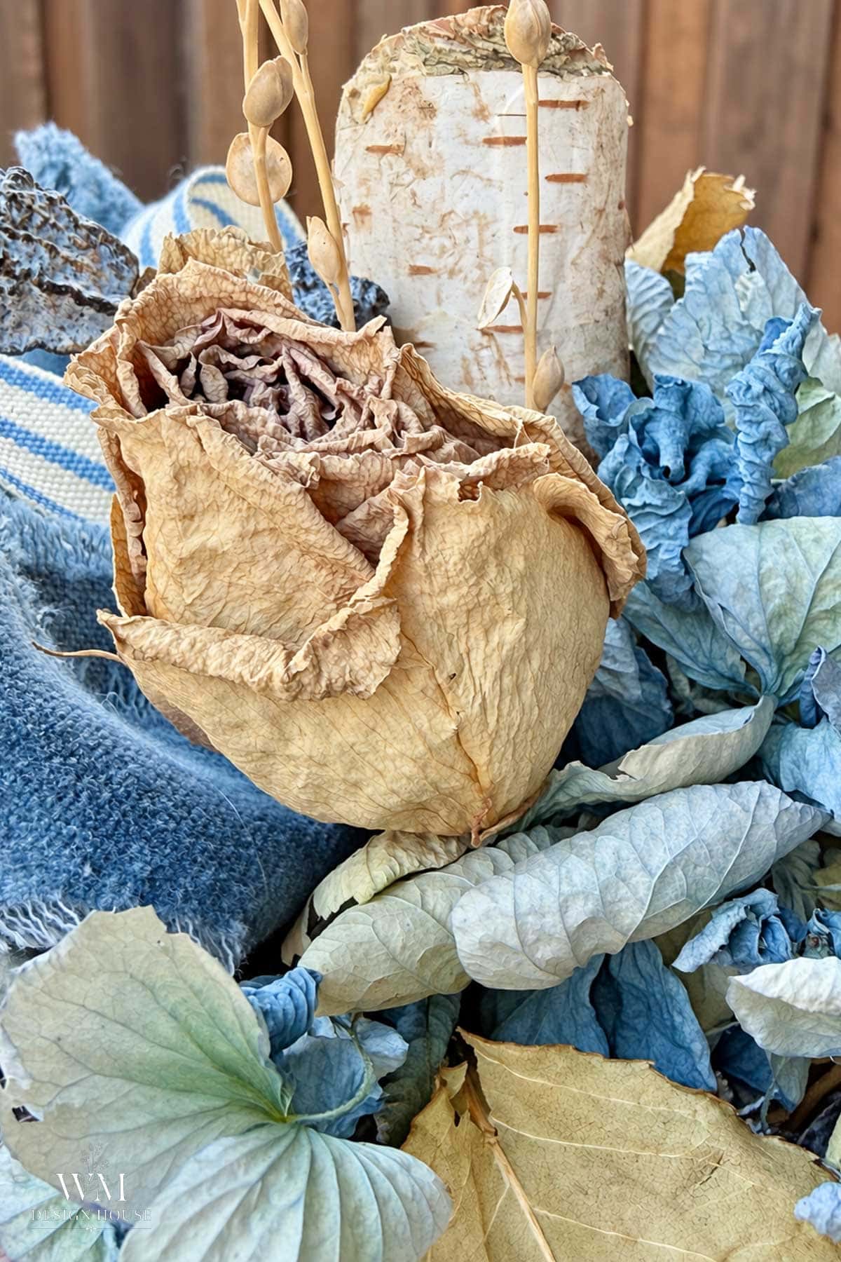 A dried tan rose nestled among blue hydrangeas and velvet ribbon topping the no sew fabric pumpkin.