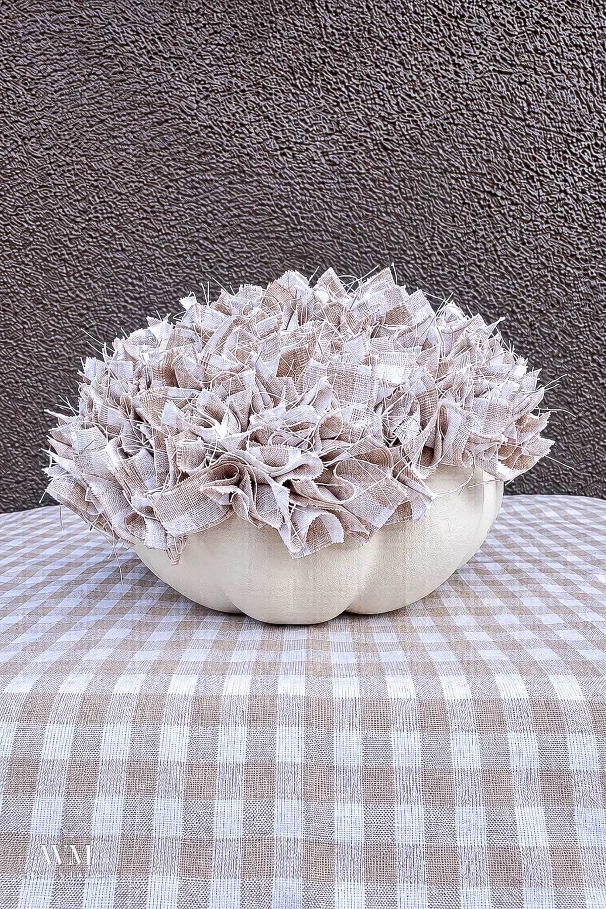 Decorative no sew fabric pumpkin in process being topped with ruffled tan and white checkered scraps.