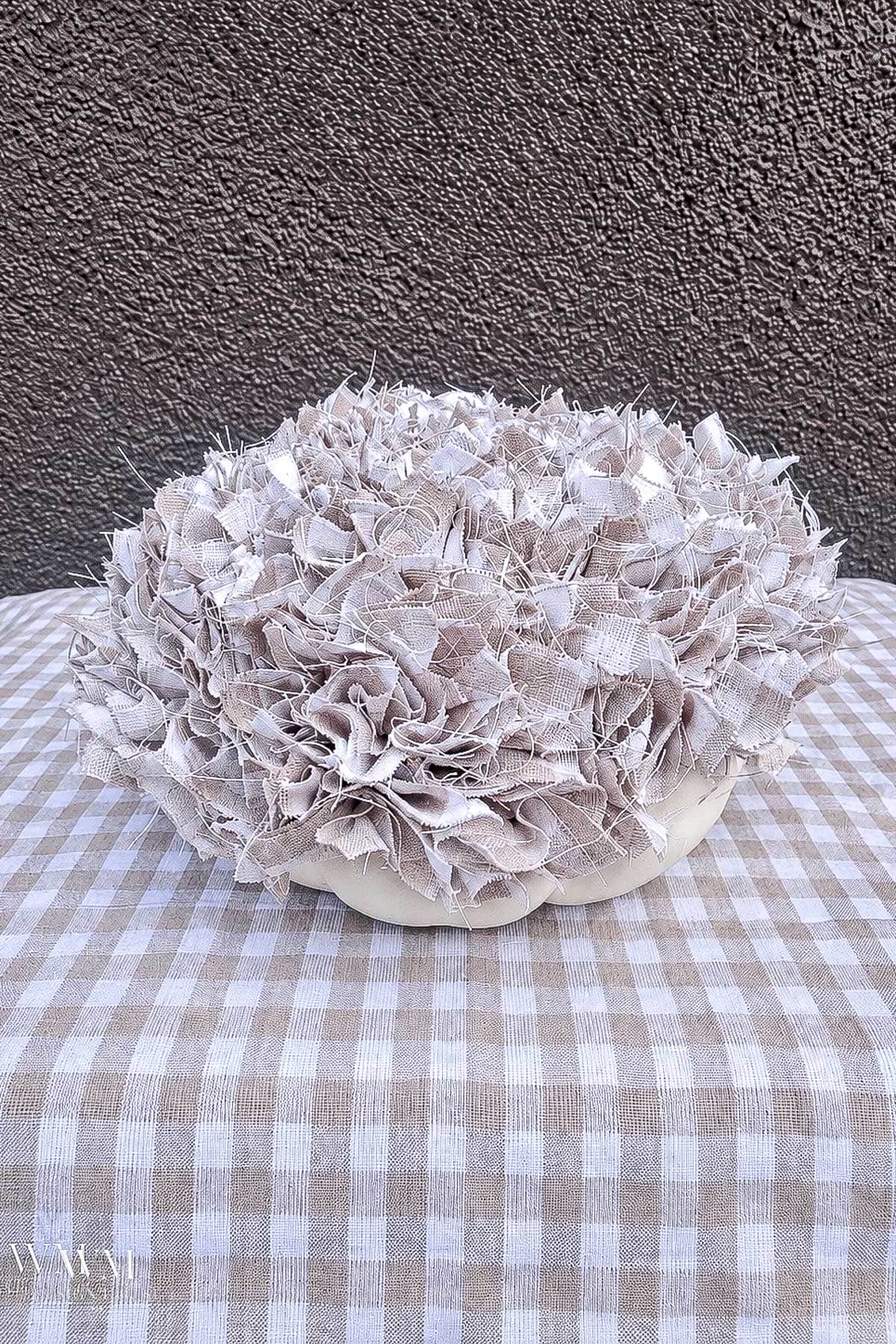 Decorative no sew fabric pumpkin in process being topped with ruffled tan and white checkered scraps.