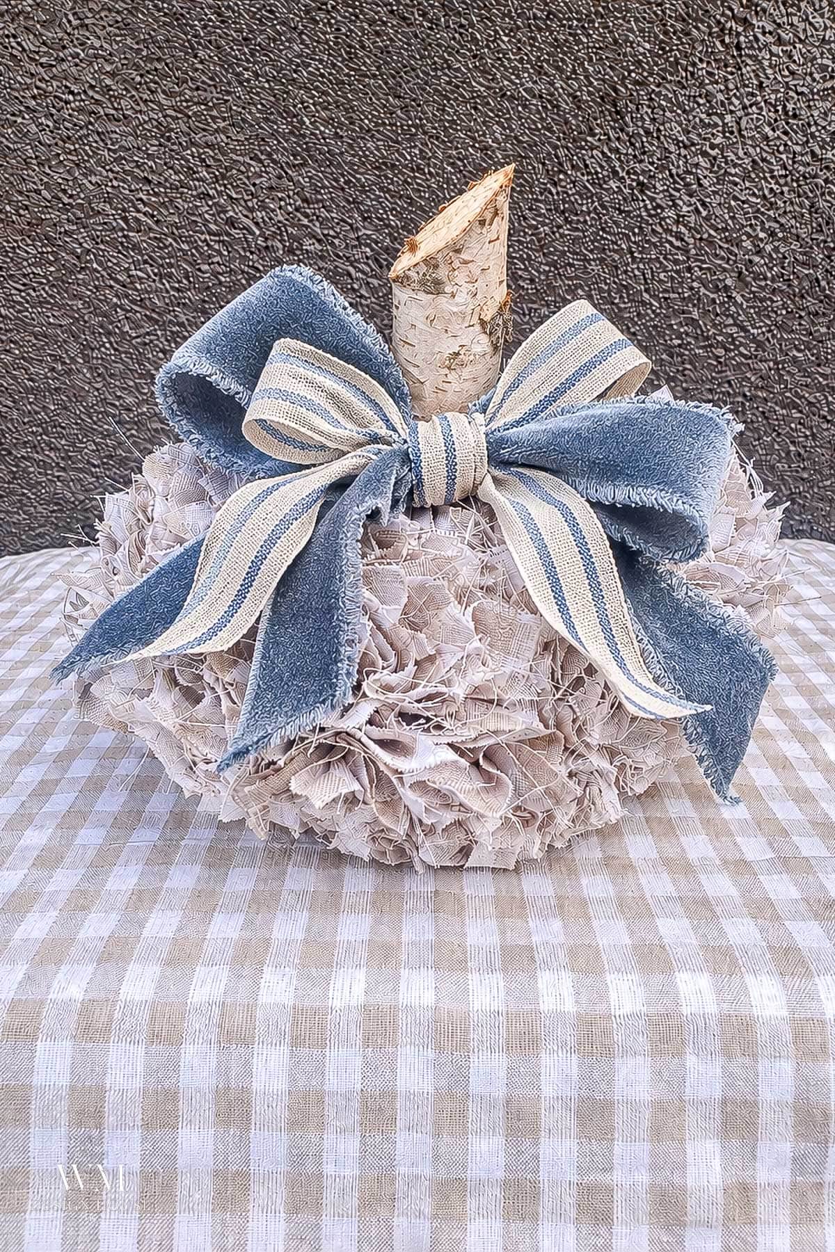 Decorative no sew fabric pumpkin with a birch wood stem, topped with a blue and beige striped ribbon bow.