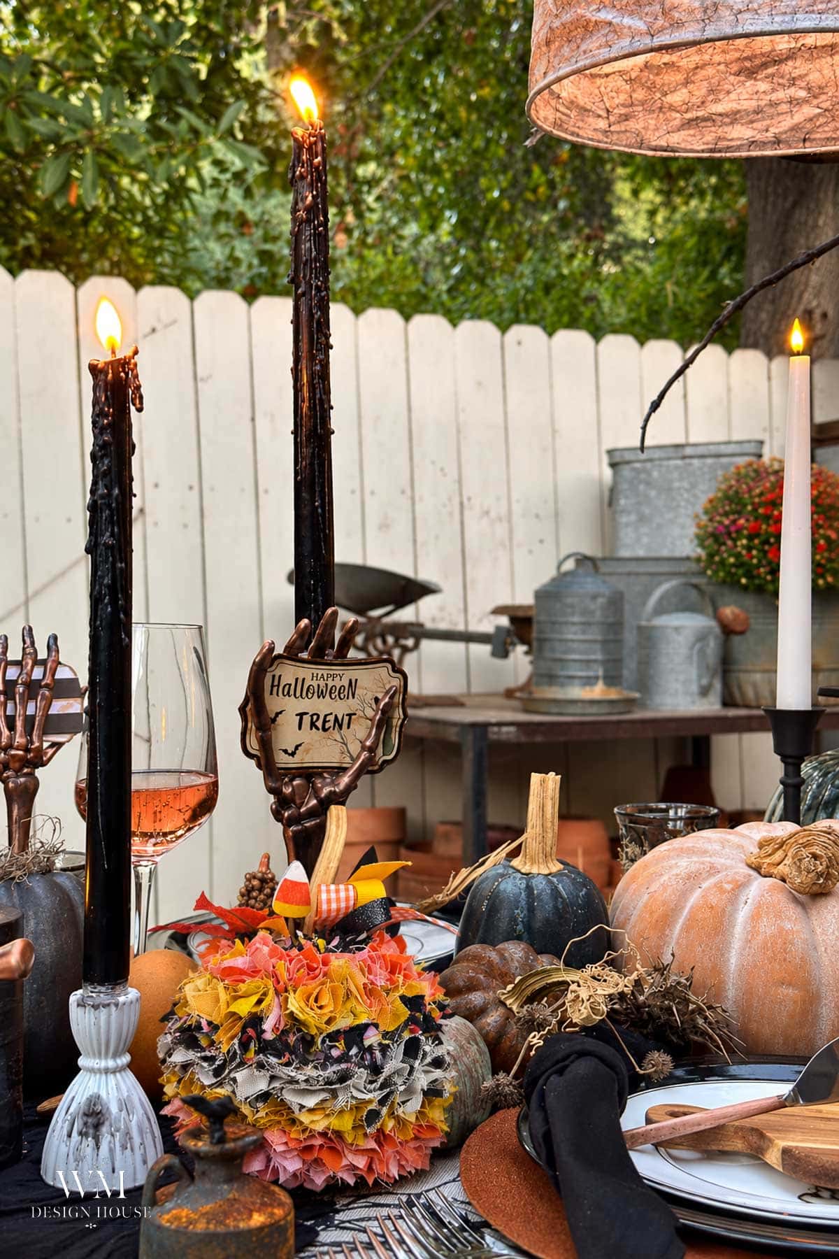 A Halloween-themed table setting featuring black taper candles, a hand-shaped candle holder with a “Happy Halloween Trent” sign, no sew fabric pumpkins, and autumn-colored fabric accents.