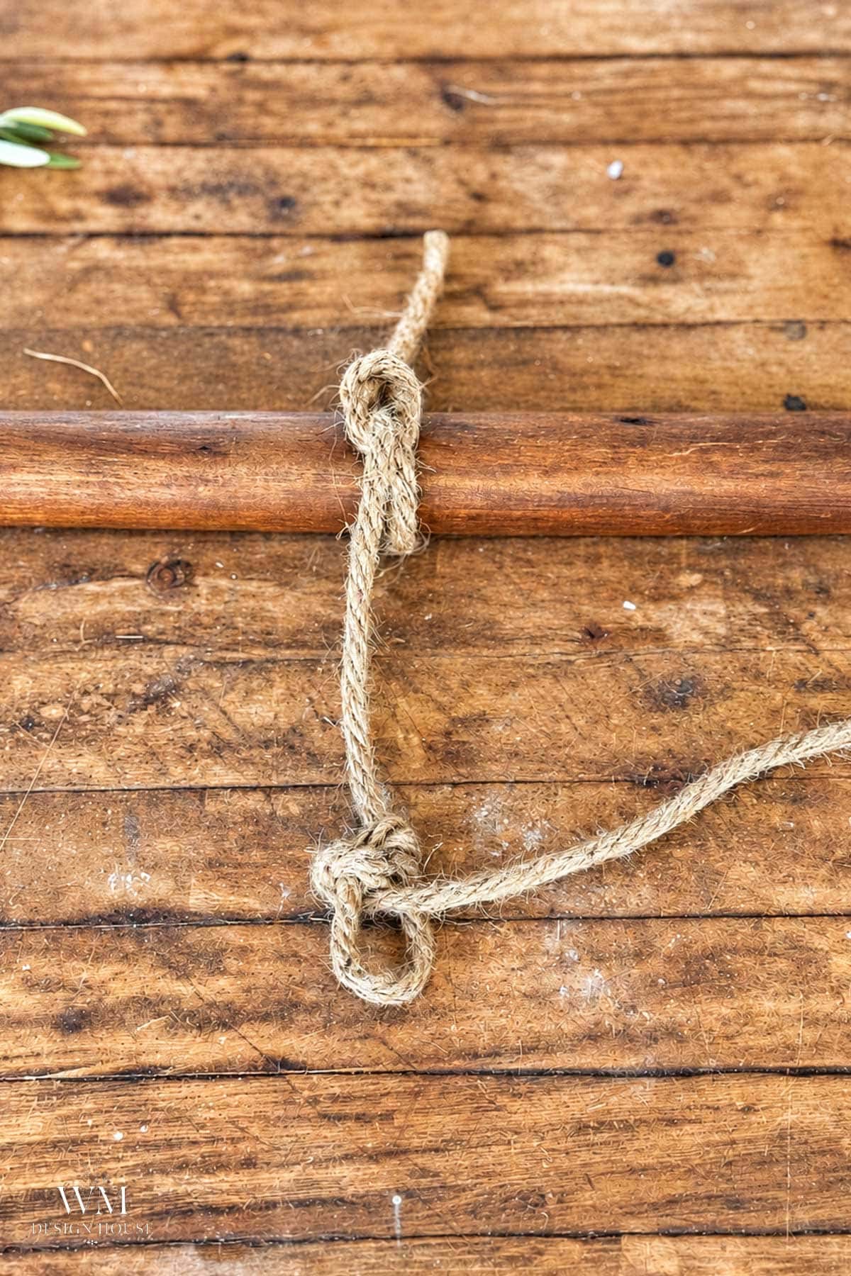 Jute rope tied in a knotted design around a horizontal wooden dowel, accented with dried orange slices to form a Christmas napkin ring.