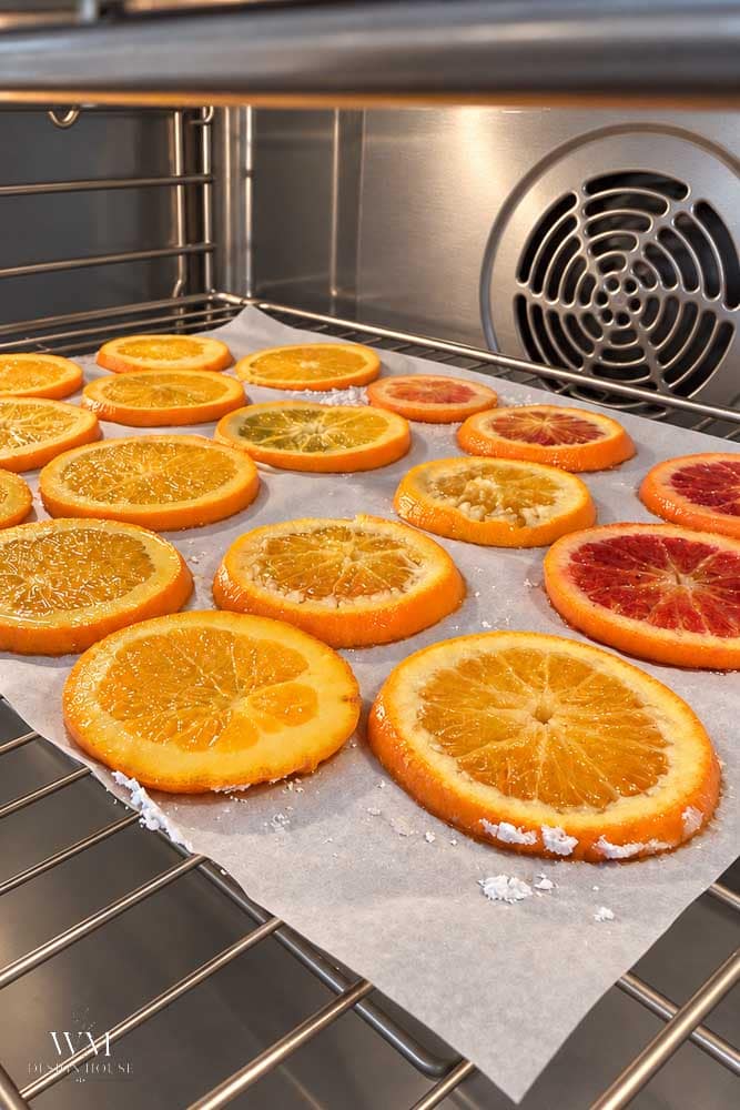 Slices of orange and blood orange covered in sugar crystals on a parchment-lined baking sheet inside an oven, becoming dried orange slices.