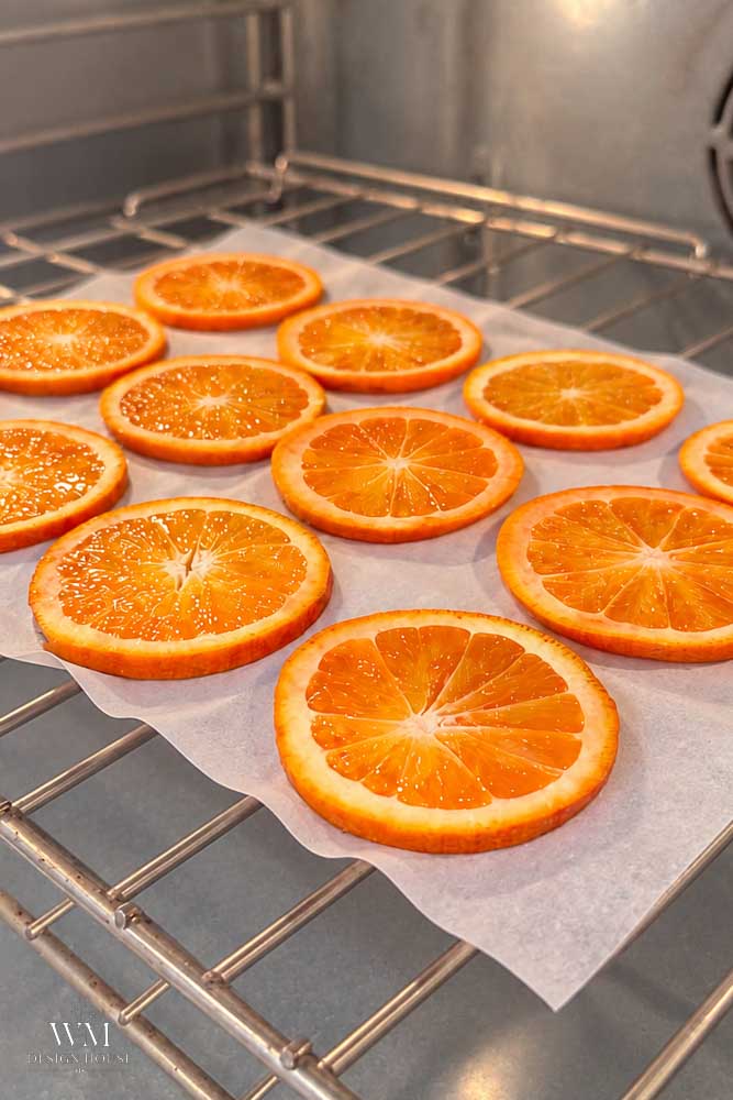 Dried orange slices arranged on parchment paper on an oven rack.