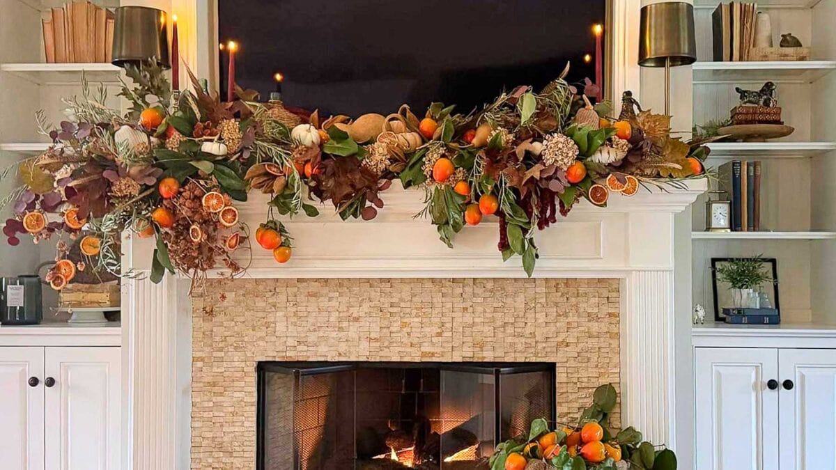 A fireplace mantel decorated with a garland of dried orange slices, greenery preserved with glycerin, and small pumpkins, surrounding a television.